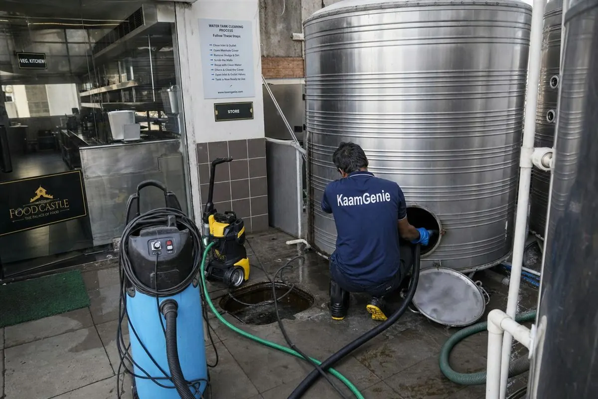 KaamGenie technician cleaning a stainless steel water storage tank at the back of a Delhi restaurant kitchen