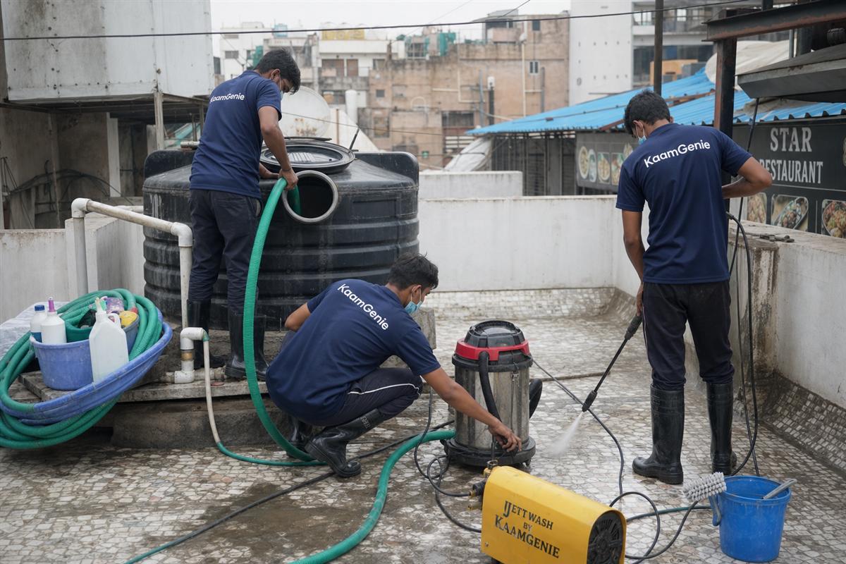 KaamGenie crew in navy uniforms cleaning a rooftop water storage tank above a Delhi restaurant kitchen