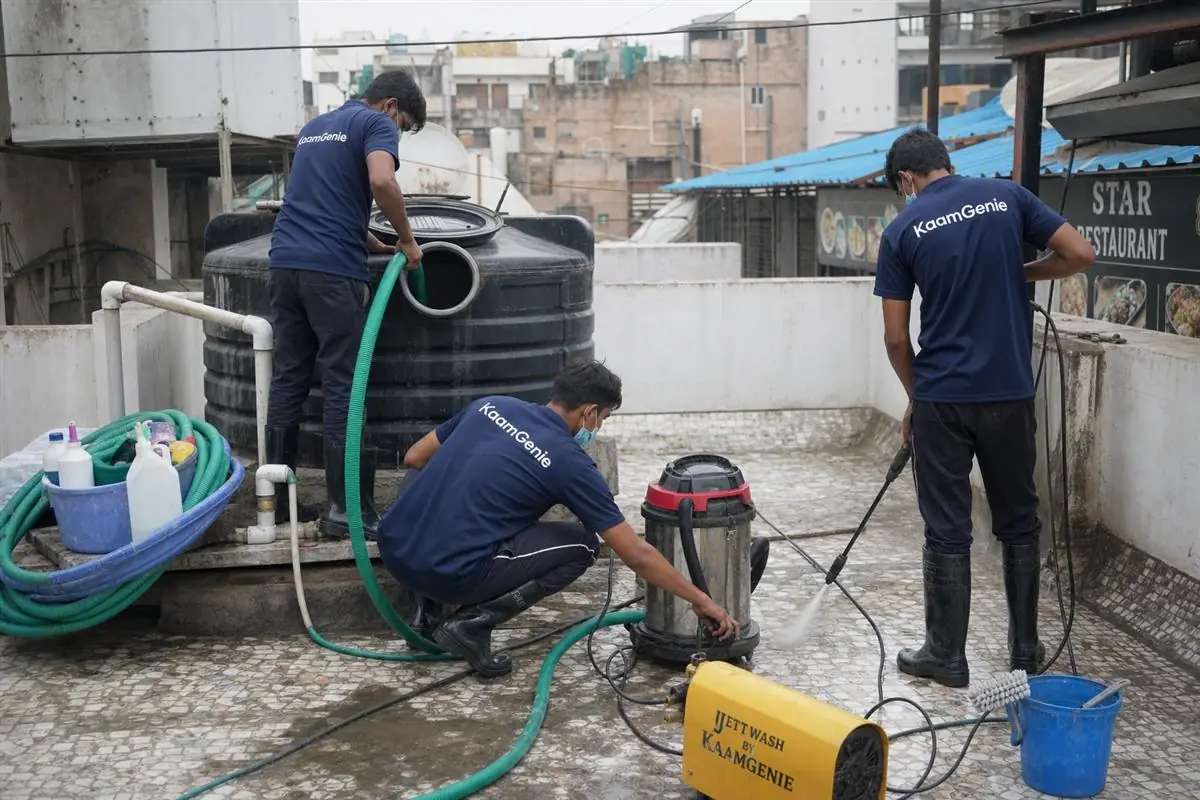 KaamGenie crew in navy uniforms cleaning a rooftop water storage tank above a Delhi restaurant kitchen