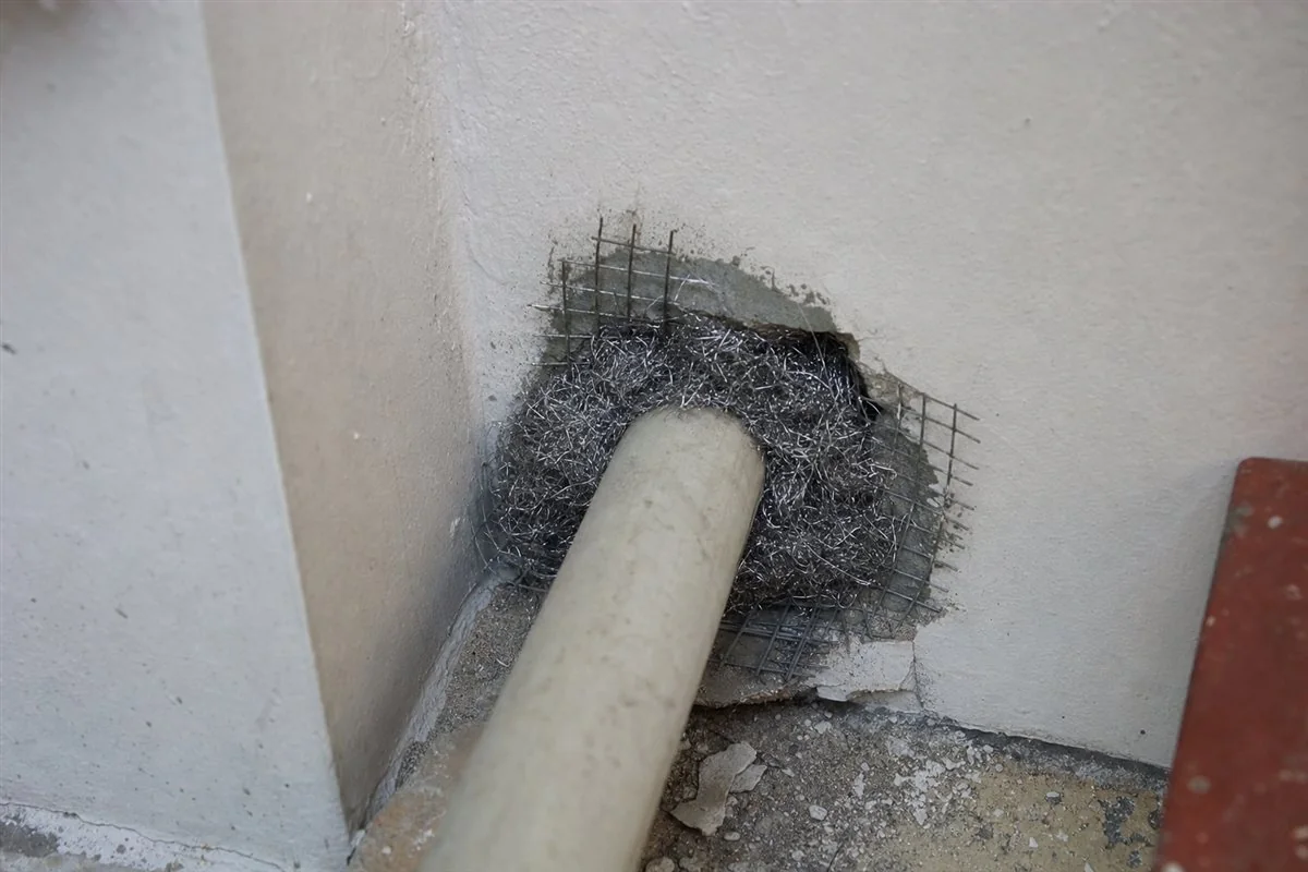 Steel wool packed into the gap around a water pipe under a Delhi kitchen sink to rodent-proof the wall penetration