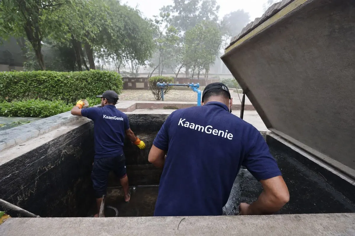 Two KaamGenie workers in navy shirts cleaning a Gurgaon society underground reservoir, producing the per-tank record an RWA keeps for audit