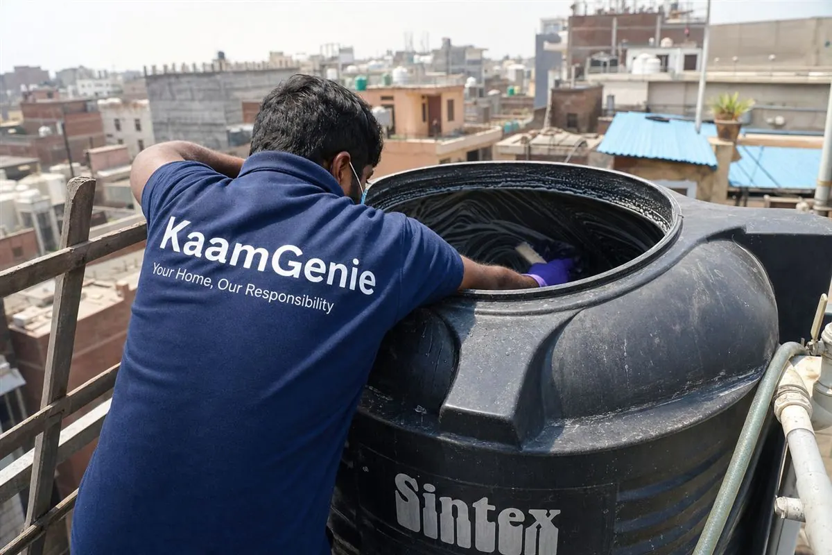 KaamGenie crew member hand-scrubbing the inside of a black Sintex plastic overhead tank on a Delhi rooftop