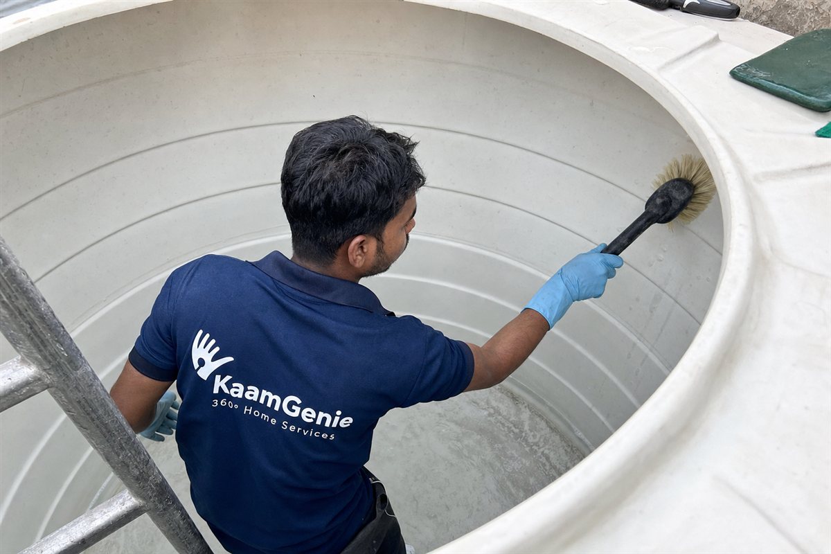 KaamGenie crew member hand-scrubbing the inside of a black Sintex plastic overhead tank on a Delhi rooftop