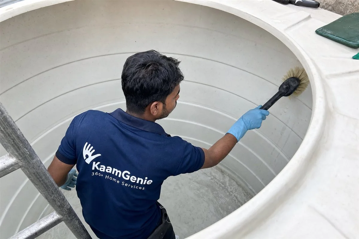KaamGenie crew member hand-scrubbing the inside of a black Sintex plastic overhead tank on a Delhi rooftop