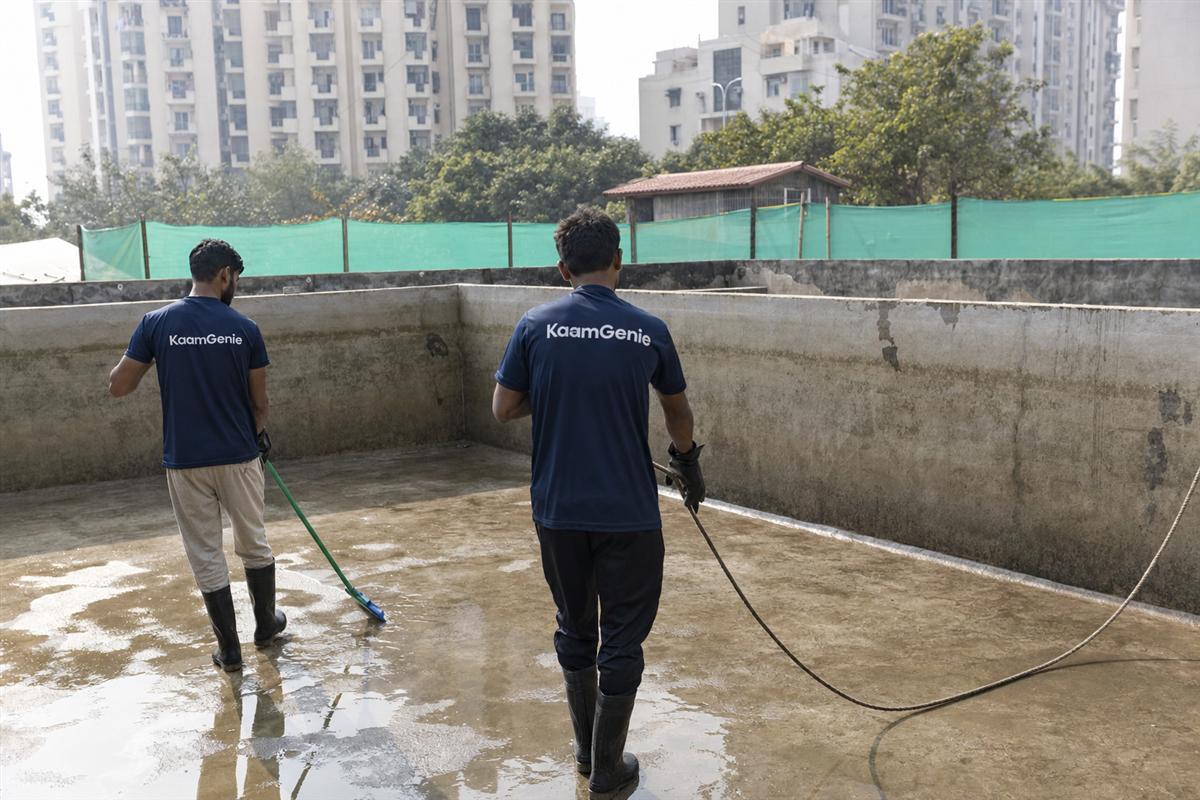 KaamGenie crew cleaning a high-rise condominium underground water reservoir in Gurgaon with residential towers behind