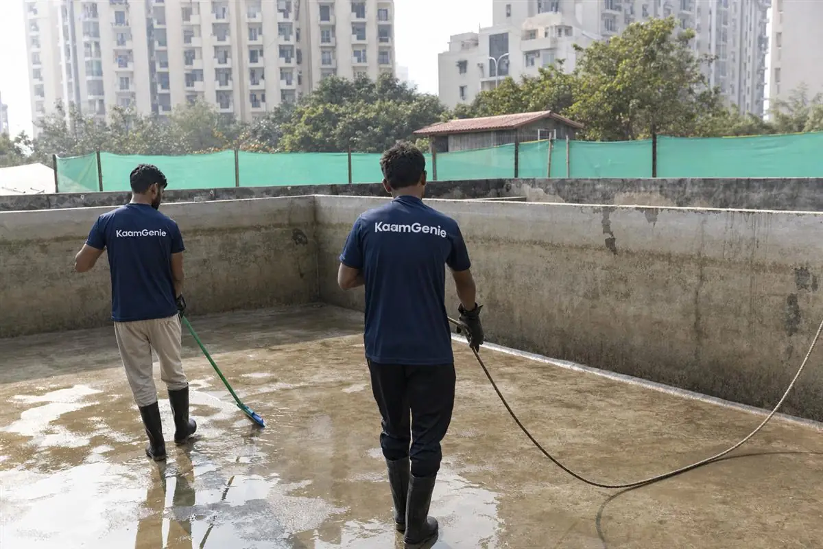 KaamGenie crew cleaning a high-rise condominium underground water reservoir in Gurgaon with residential towers behind