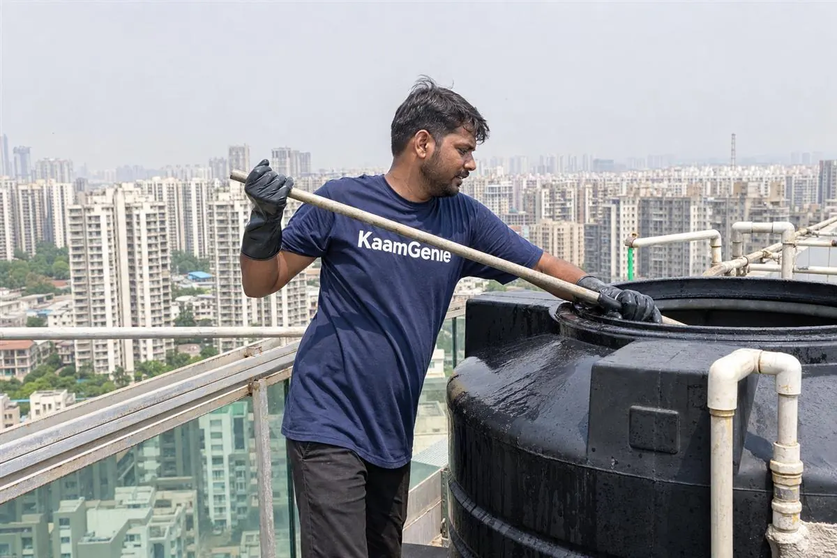 Diagram-style photo of a Noida high-rise water system - underground reservoir at the base feeding pumps that lift water to rooftop overhead tanks on each tower