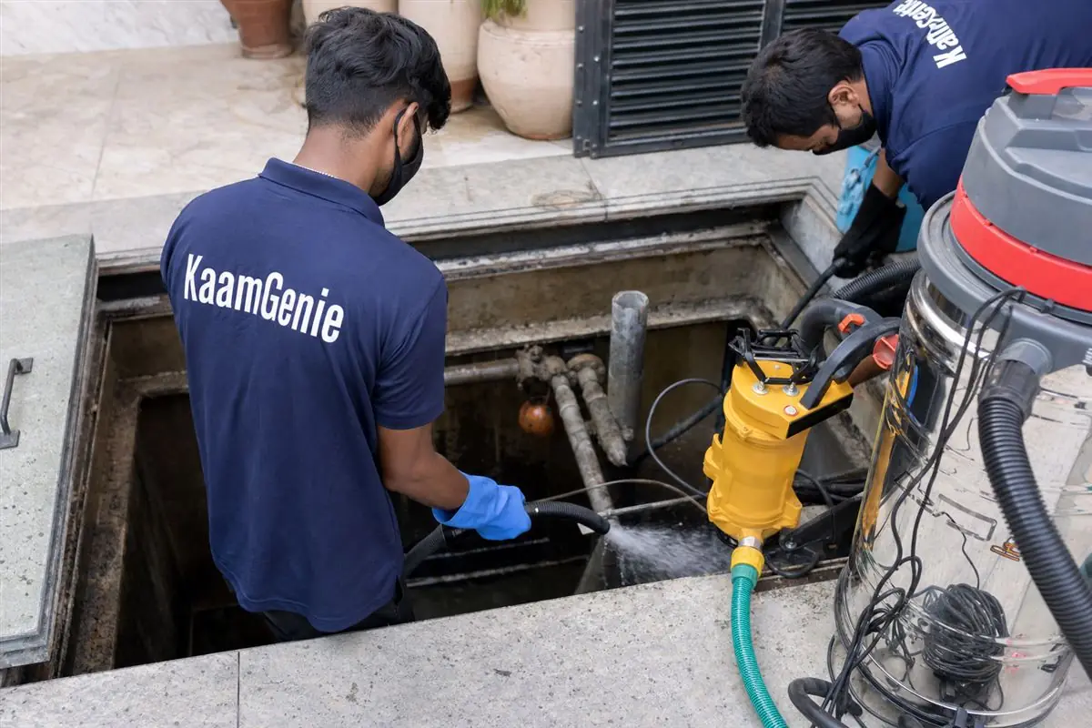 KaamGenie technician in navy uniform cleaning a large underground sump tank at a Delhi kothi with a pump and hose