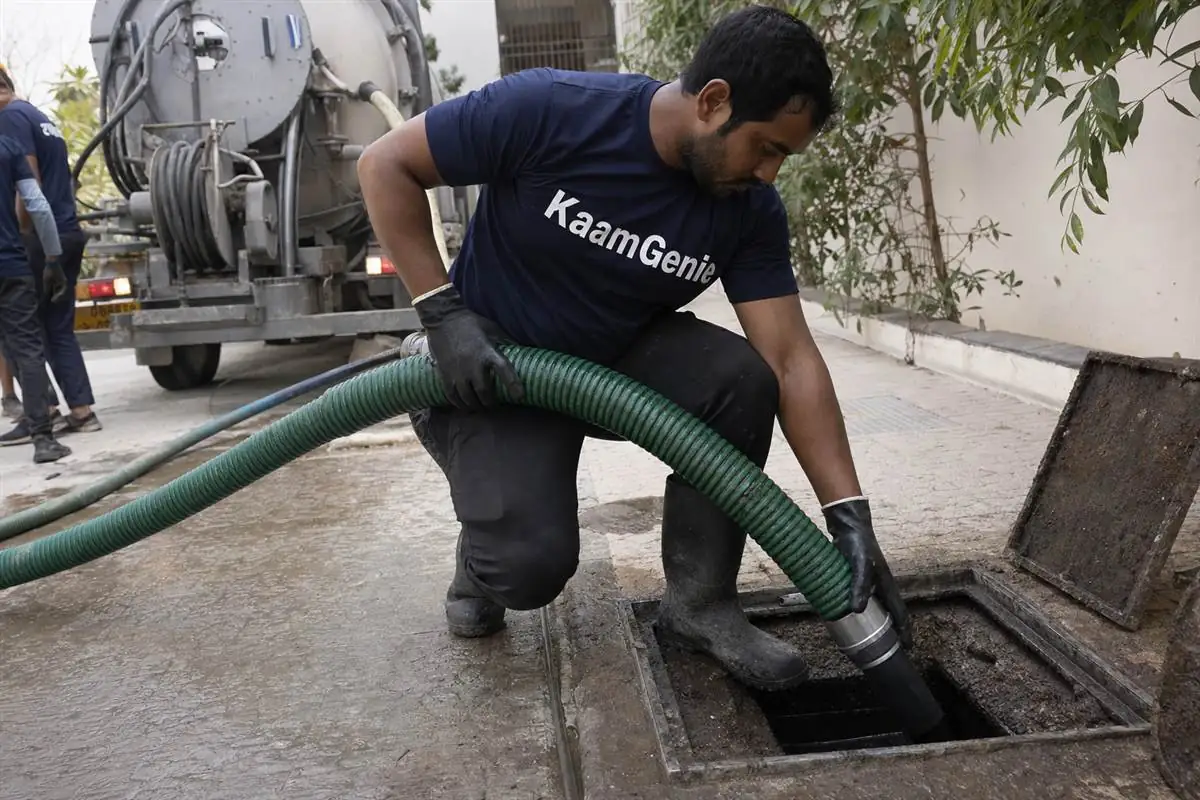A KaamGenie crew member inside a large underground reservoir at a Gurgaon society, scooping a thick layer of silt and sludge off the floor into a bucket