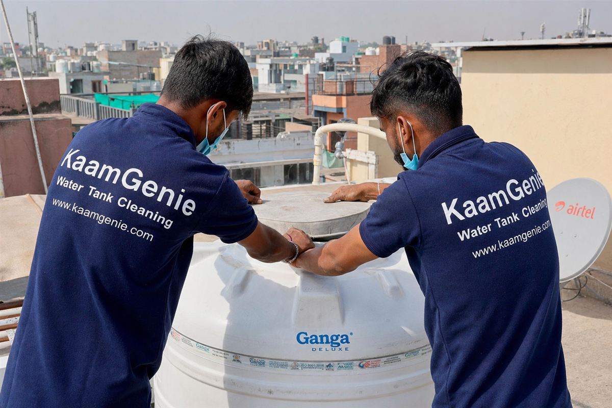 KaamGenie crew in navy-blue branded shirts sealing the lid of a rooftop water tank after cleaning, in a Delhi residential setting