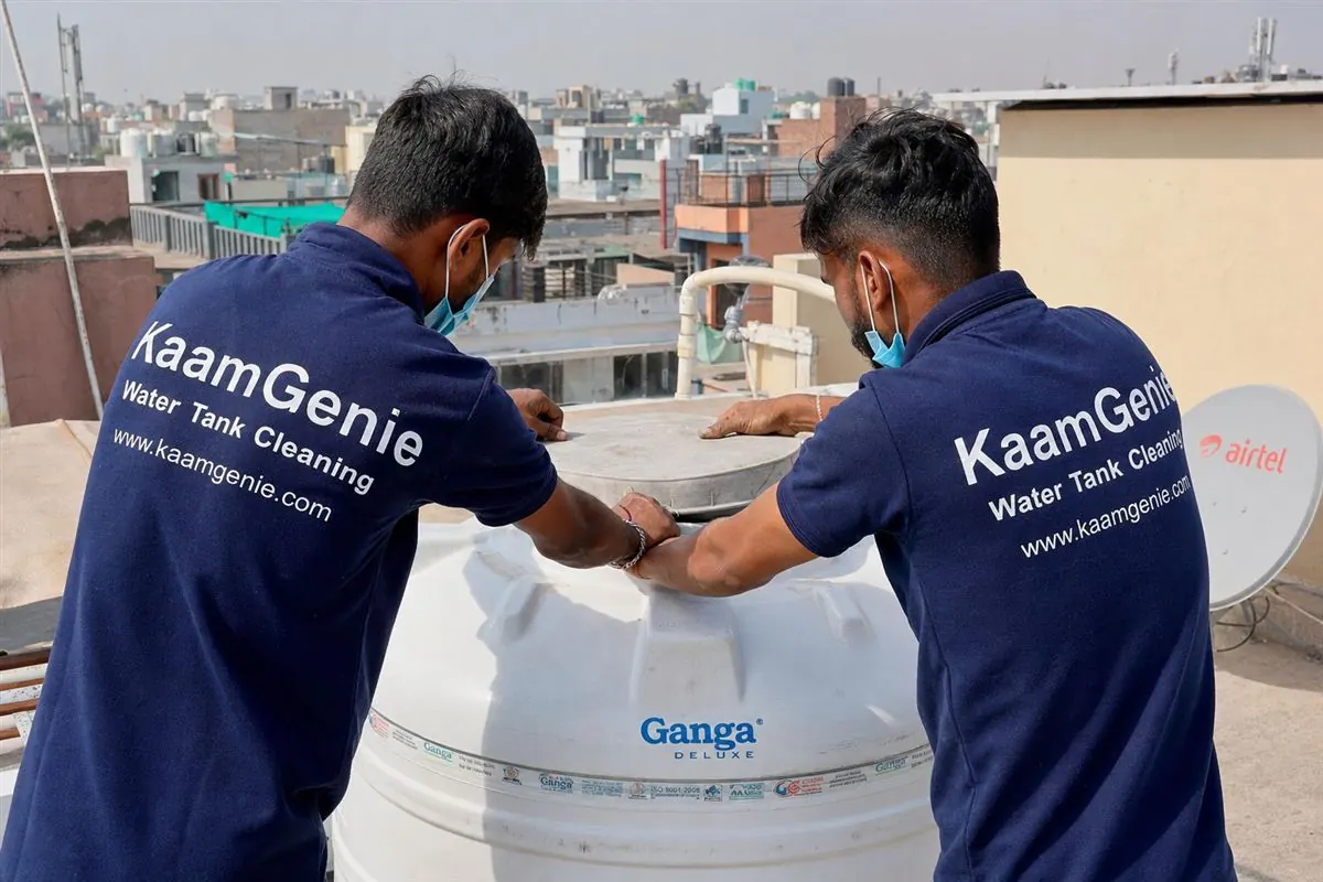 KaamGenie crew in navy-blue branded shirts sealing the lid of a rooftop water tank after cleaning, in a Delhi residential setting