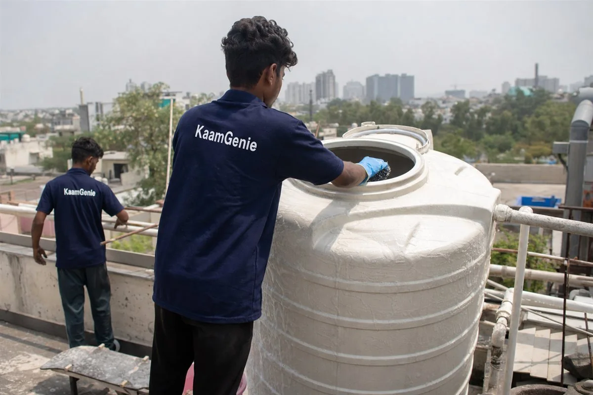 A KaamGenie worker in a navy shirt scrubbing the inside of a rooftop water tank at a Gurgaon home