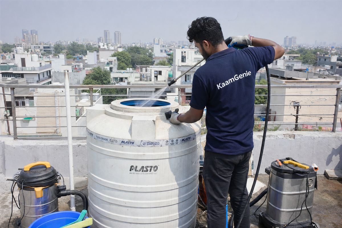 KaamGenie technician cleaning an overhead water tank on the terrace of a Delhi rental apartment building