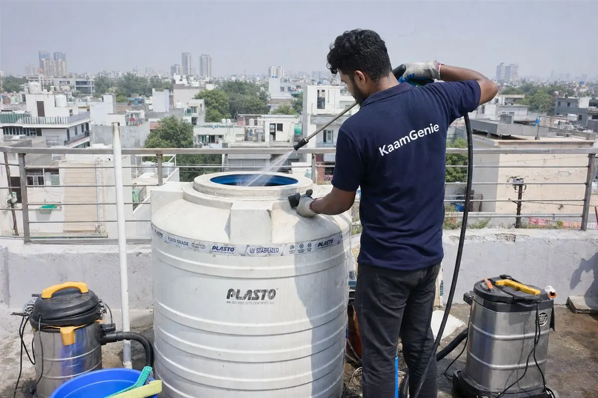 KaamGenie technician cleaning an overhead water tank on the terrace of a Delhi rental apartment building