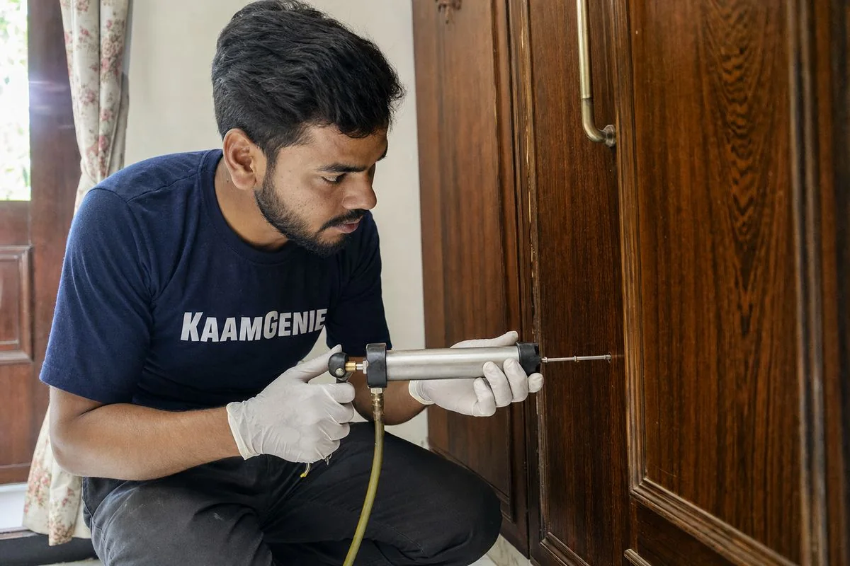 KaamGenie technician injecting anti-termite chemical into a small drilled hole in a wooden almirah in a Delhi home