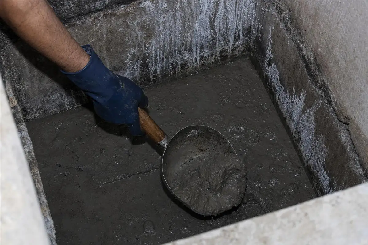 KaamGenie crew member inside an underground reservoir manually scooping settled sludge into a bucket while a colleague stands by at the opening