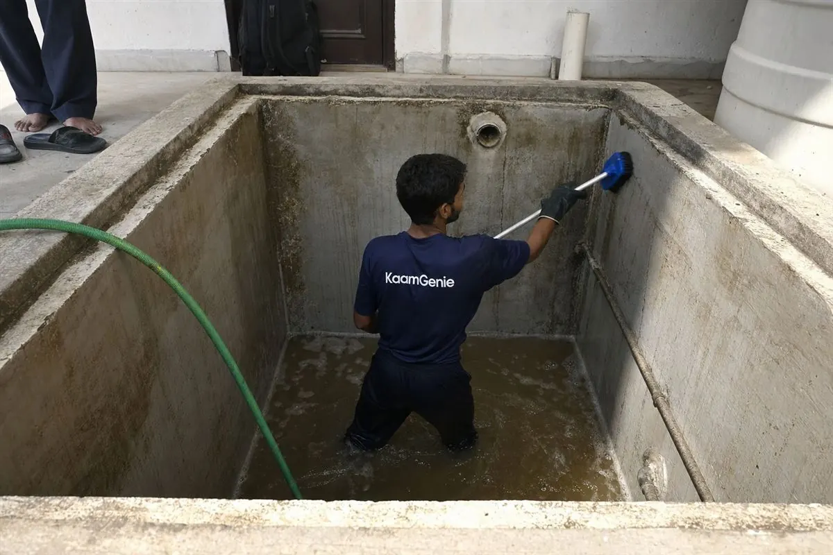 A KaamGenie worker in a navy shirt cleaning a large private underground sump at a South Delhi villa
