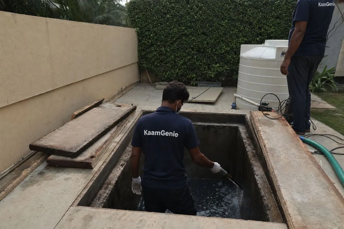 KaamGenie crew member in a navy shirt cleaning a private underground water sump at a Gurgaon villa, with confined-space equipment around the opening