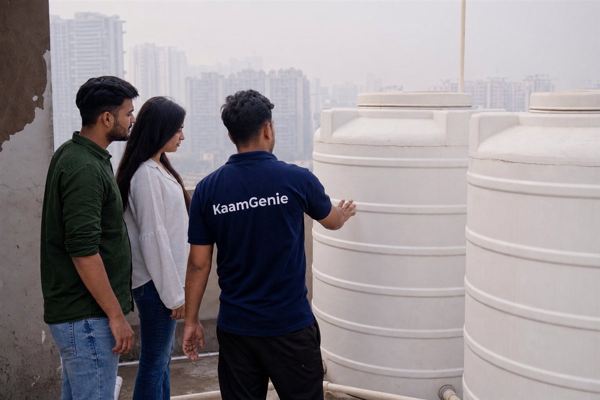 A young couple with a KaamGenie worker in a navy shirt inspecting the rooftop tank of a newly handed-over Gurgaon flat before moving in