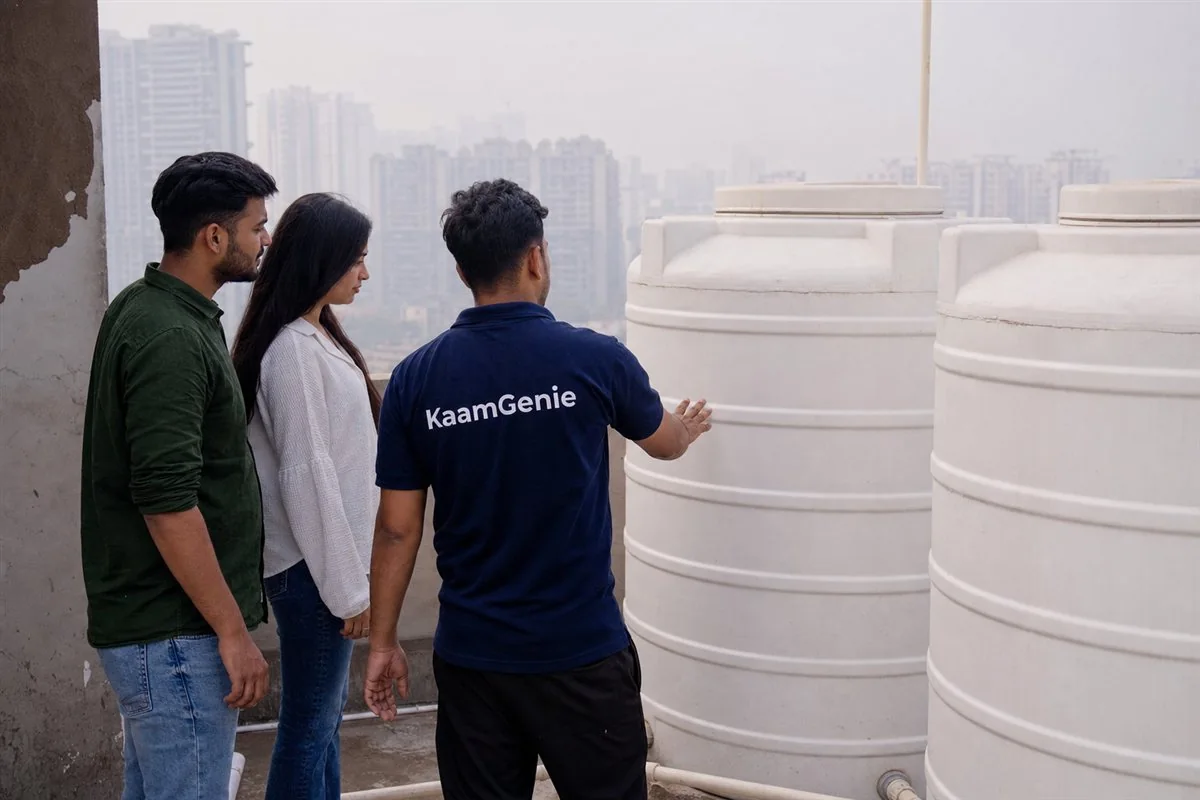 A young couple with a KaamGenie worker in a navy shirt inspecting the rooftop tank of a newly handed-over Gurgaon flat before moving in