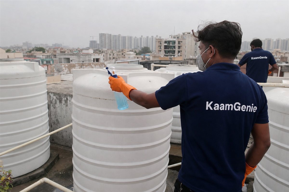 A KaamGenie worker in a navy shirt disinfecting a freshly cleaned water tank before a family moves into a Noida flat