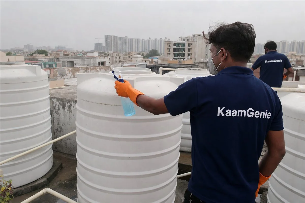 A KaamGenie worker in a navy shirt disinfecting a freshly cleaned water tank before a family moves into a Noida flat