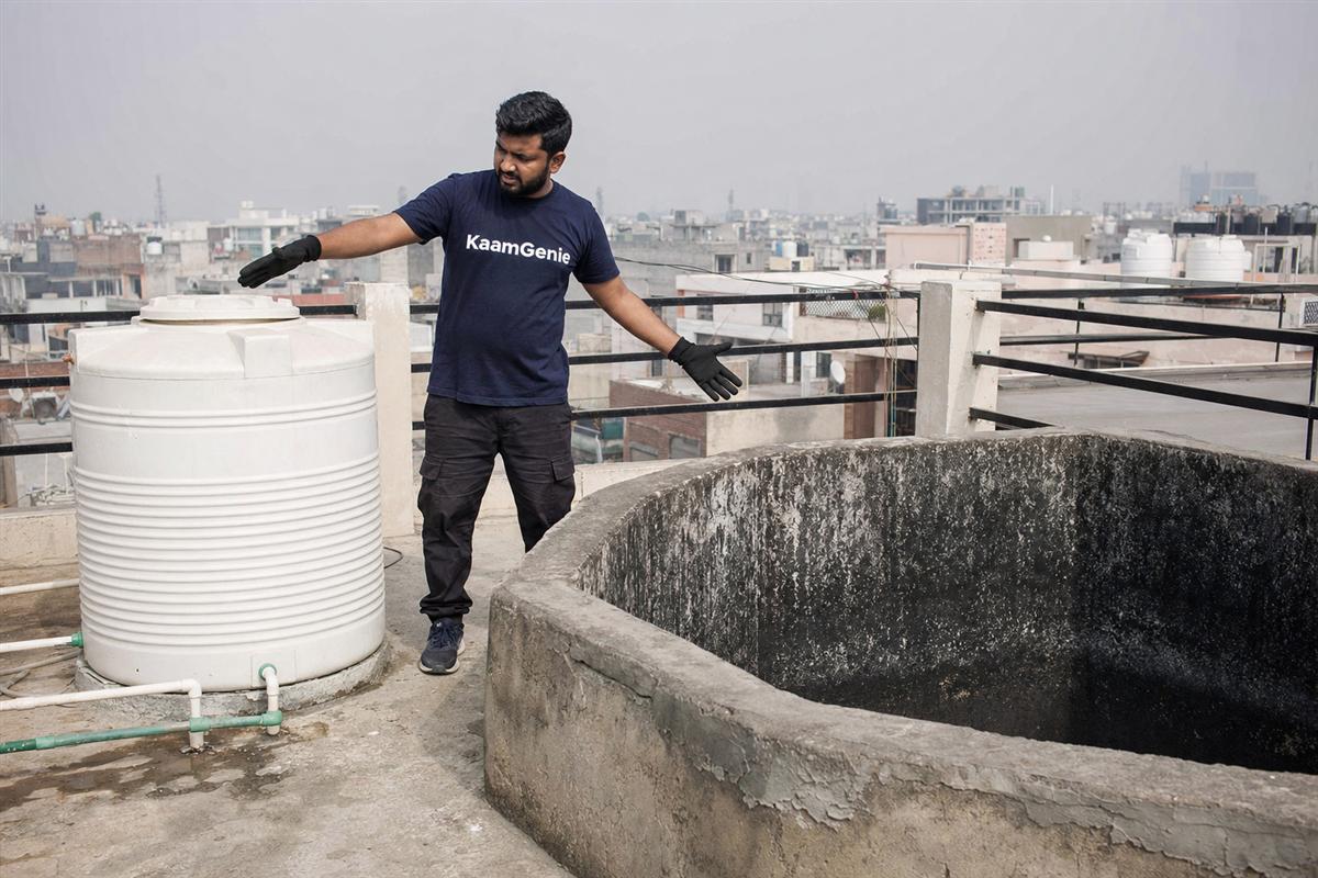 A KaamGenie crew member scrubbing the interior of a rooftop overhead water tank, before-photos being taken for documentation
