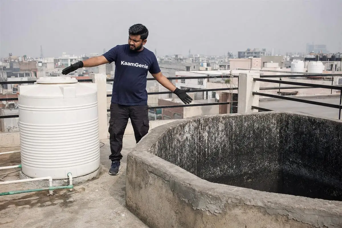 A KaamGenie crew member scrubbing the interior of a rooftop overhead water tank, before-photos being taken for documentation