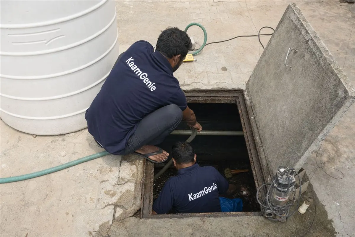 Two KaamGenie crew members in navy shirts cleaning a Gurgaon underground sump with a submersible pump and cleaning equipment around them