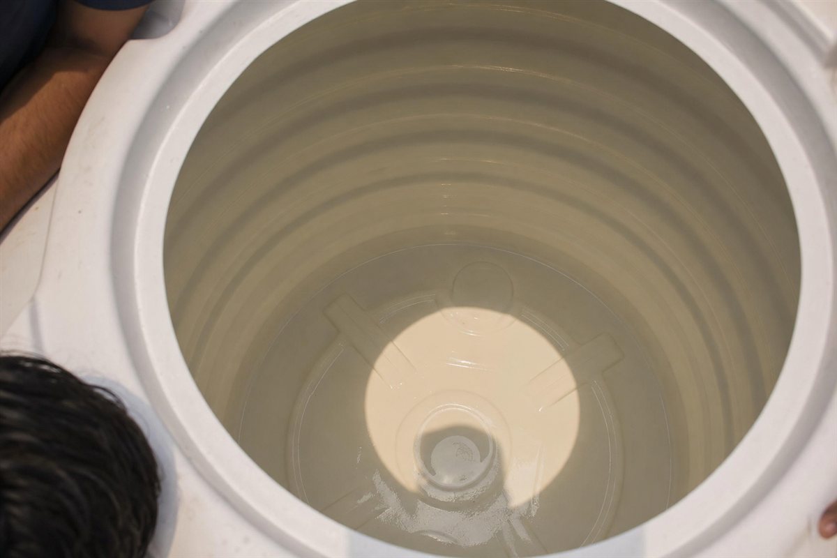 Close-up of a sparkling clean plastic water tank interior in a Noida flat immediately after a KaamGenie cleaning, walls and floor free of sludge and scale