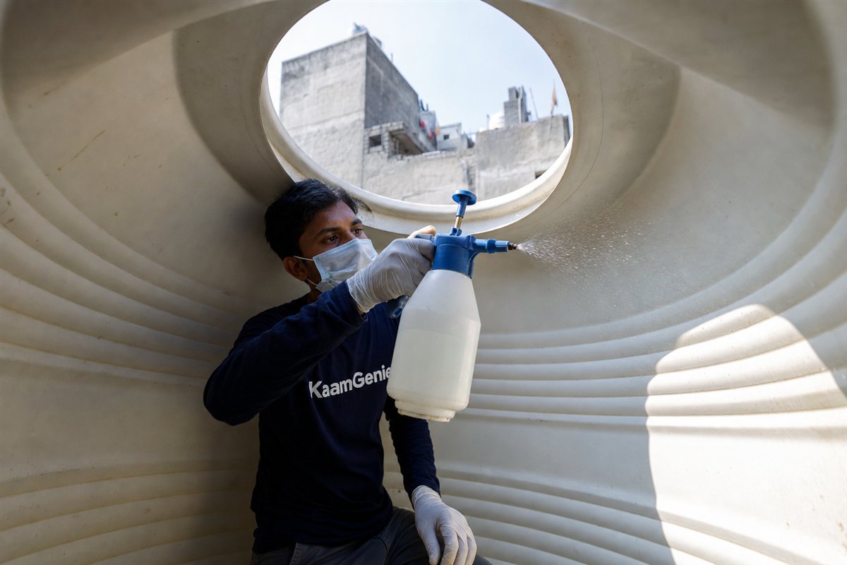 KaamGenie technician spraying measured food-grade sodium hypochlorite solution across the interior walls of a cleaned plastic water tank in Delhi