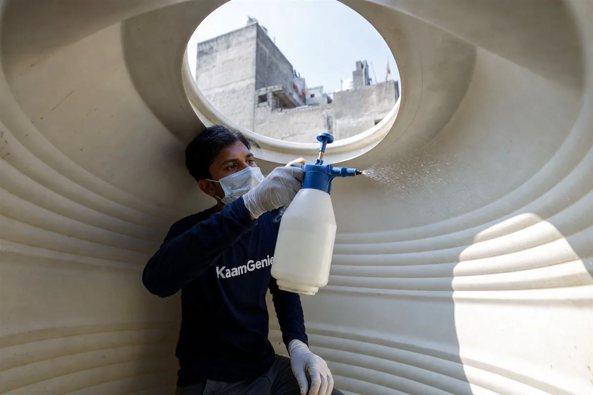 KaamGenie technician spraying measured food-grade sodium hypochlorite solution across the interior walls of a cleaned plastic water tank in Delhi