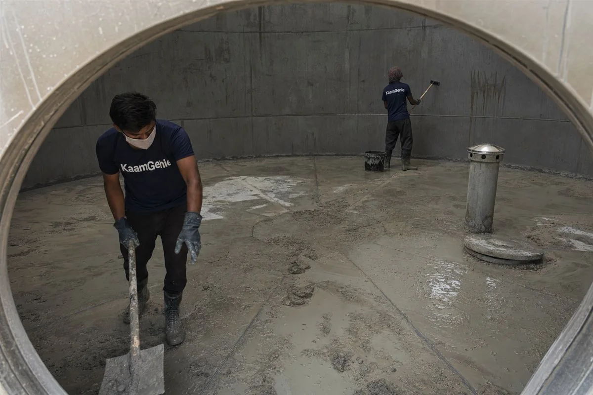 KaamGenie crew scooping grey cement slurry and construction debris from the bottom of a newly built underground water reservoir in a New Gurgaon high-rise
