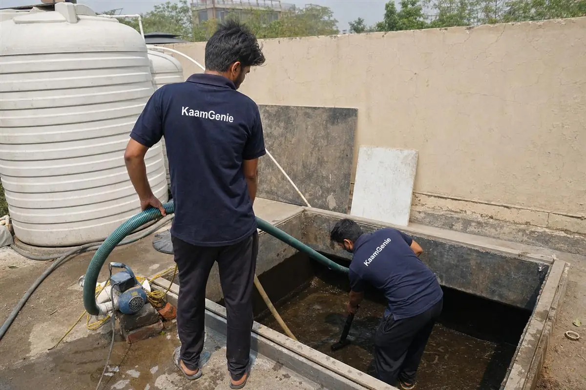 A KaamGenie worker in a navy shirt vacuuming sandy sediment from the floor of an underground reservoir at a Greater Noida plotted kothi