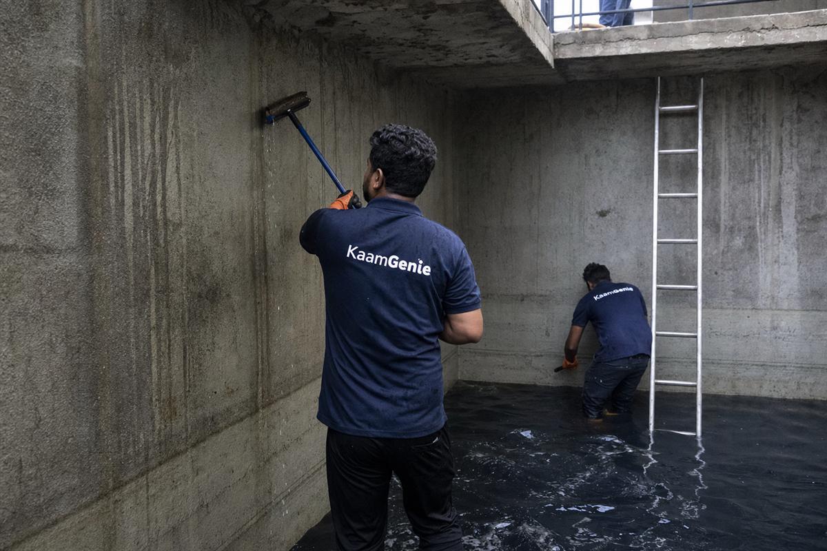 Two KaamGenie workers in navy shirts cleaning a large basement underground reservoir in a luxury Jaypee Wish Town condominium
