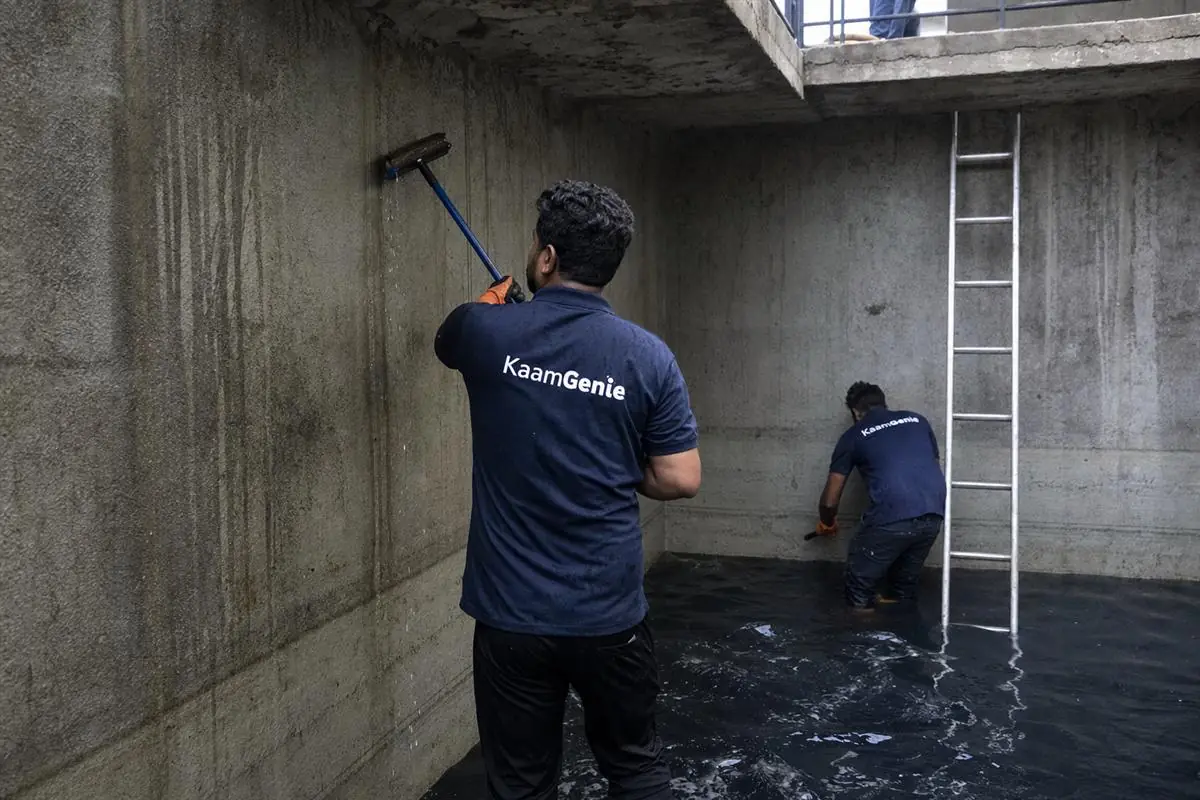 Two KaamGenie workers in navy shirts cleaning a large basement underground reservoir in a luxury Jaypee Wish Town condominium