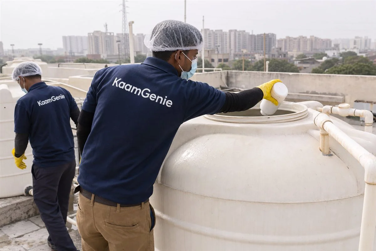A KaamGenie worker in a navy shirt disinfecting a clean rooftop tower tank on a Jaypee Wish Town building