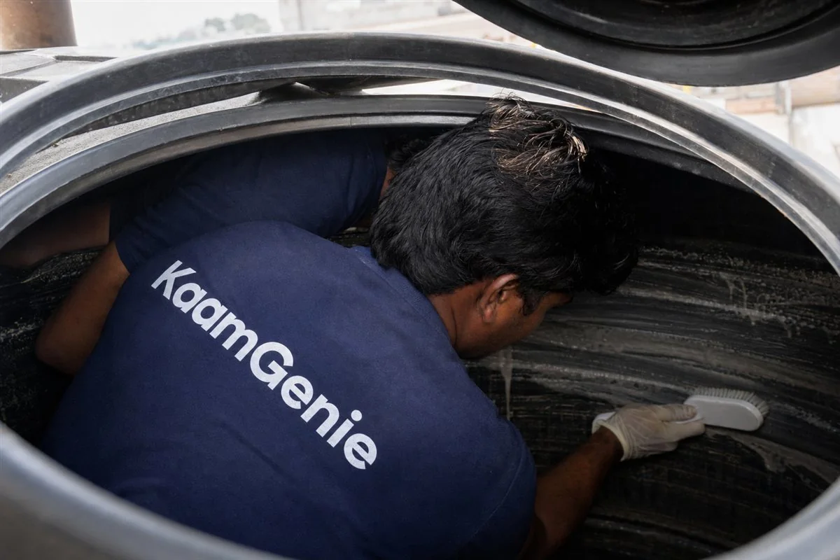 KaamGenie technician inside a plastic water tank manually scrubbing the wall with a food-grade nylon brush on a Delhi rooftop