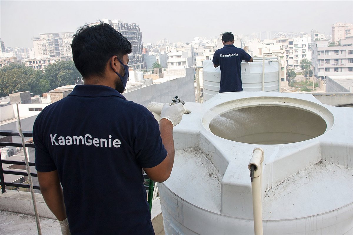KaamGenie worker in a navy shirt disinfecting a freshly cleaned rooftop tower tank in a New Gurgaon high-rise after the first clean