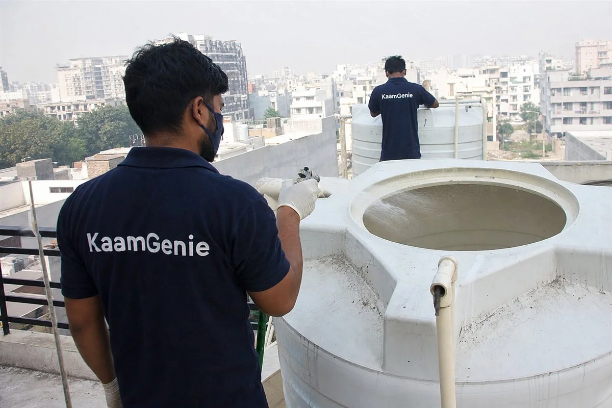 KaamGenie worker in a navy shirt disinfecting a freshly cleaned rooftop tower tank in a New Gurgaon high-rise after the first clean
