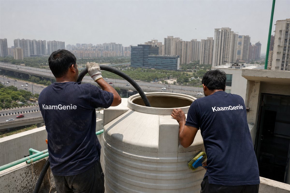 KaamGenie crew cleaning a rooftop water tank on a tall Noida Expressway high-rise tower with the expressway and other towers behind