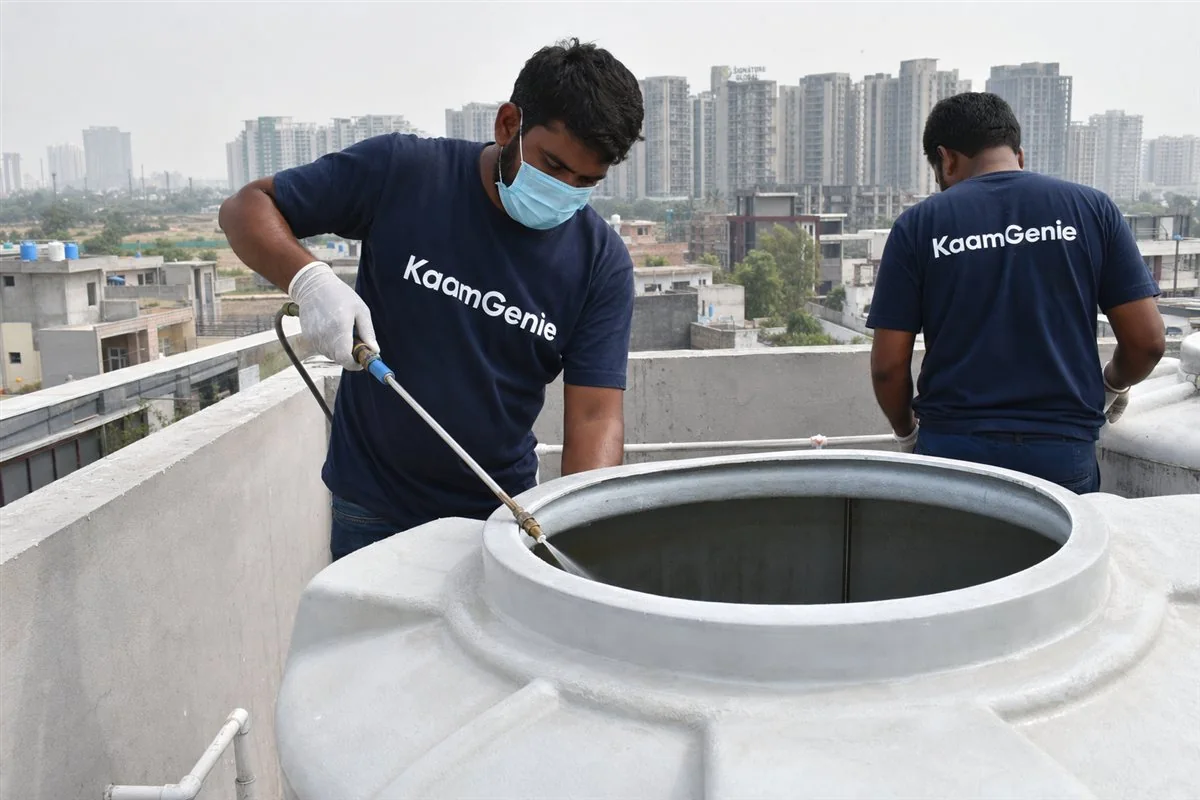 KaamGenie worker in a navy shirt disinfecting the inside walls of a clean water tank in Gurgaon with a food-grade chlorine spray