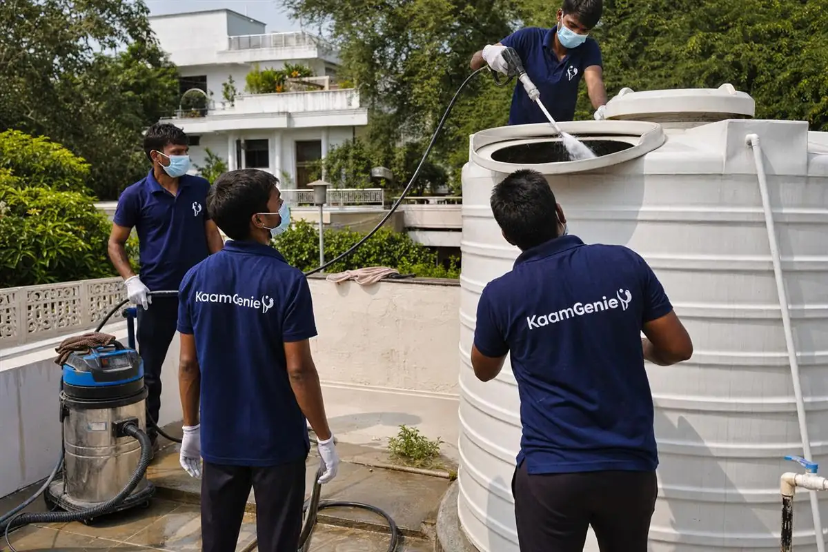 KaamGenie crew in navy shirts cleaning an overhead water tank on a South Delhi kothi rooftop in Greater Kailash