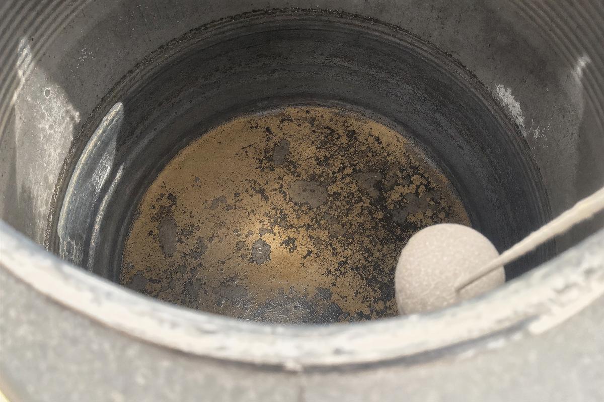 Close-up of dark sediment and sludge inside a Gurgaon storage water tank that feeds the whole home, with a gloved hand pointing