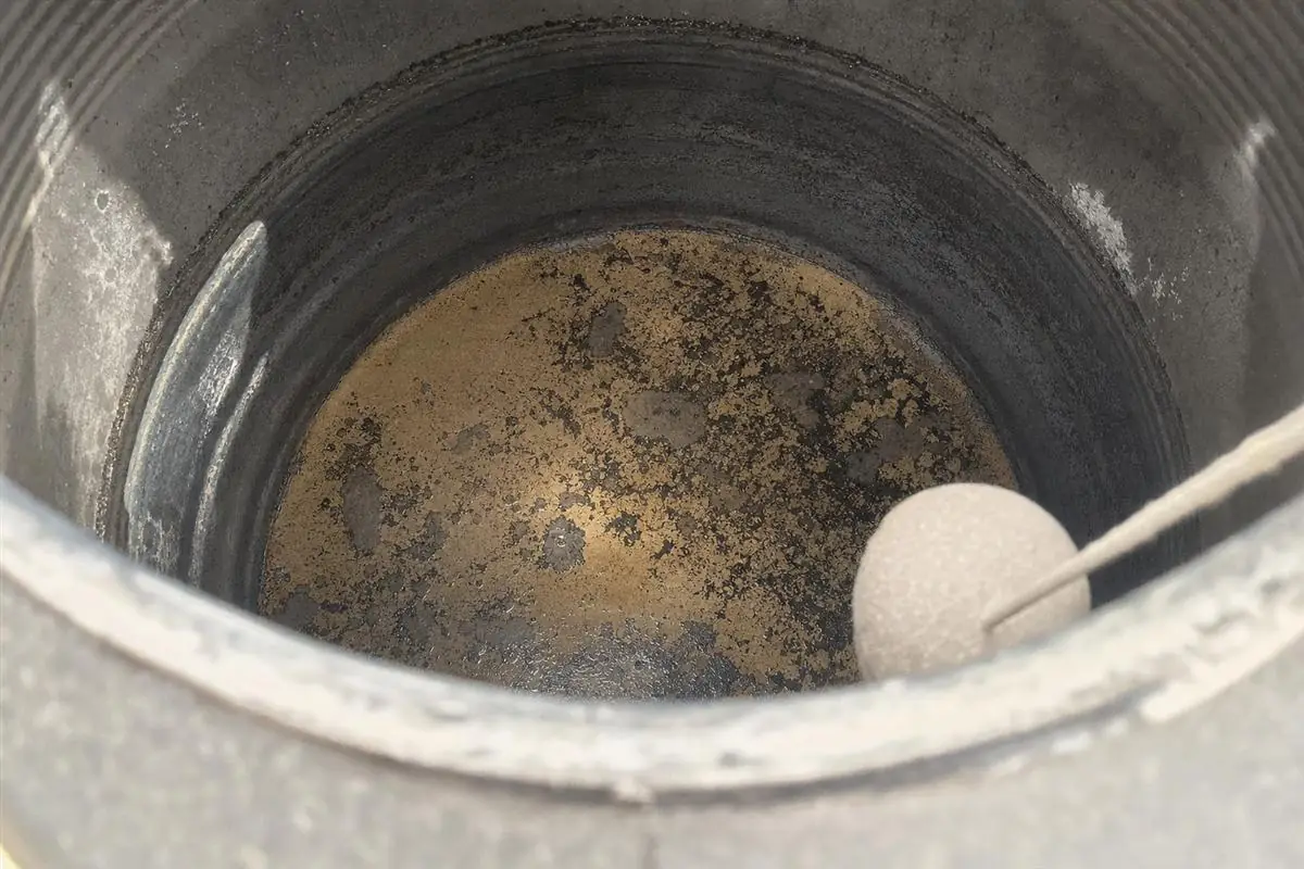 Close-up of dark sediment and sludge inside a Gurgaon storage water tank that feeds the whole home, with a gloved hand pointing