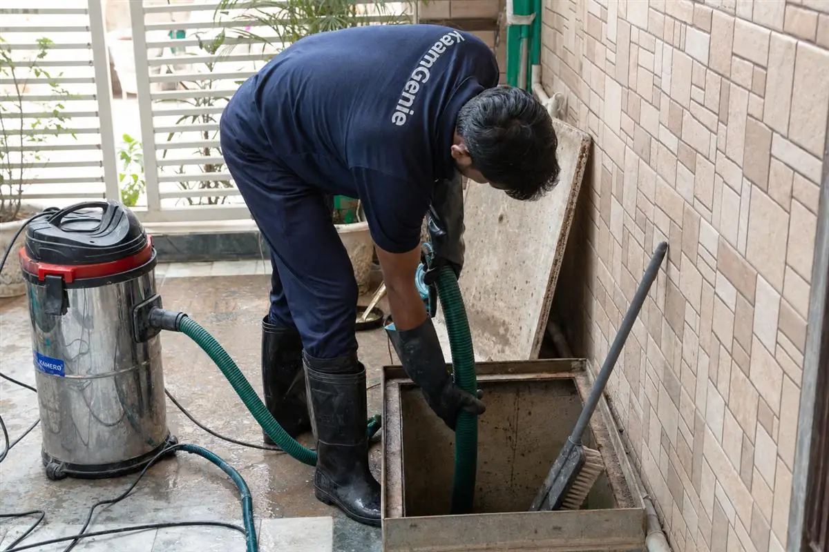 KaamGenie technician in navy uniform vacuuming sludge from an underground sump in a Janakpuri West Delhi home