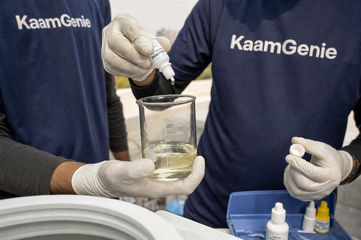 Close-up of gloved hands measuring food-grade chlorine solution in a beaker beside a clean water tank in Gurgaon