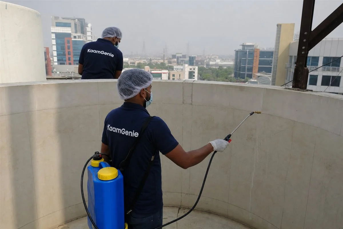 KaamGenie crew member in a navy shirt spraying food-grade disinfectant on the clean interior walls of a water tank in Gurgaon