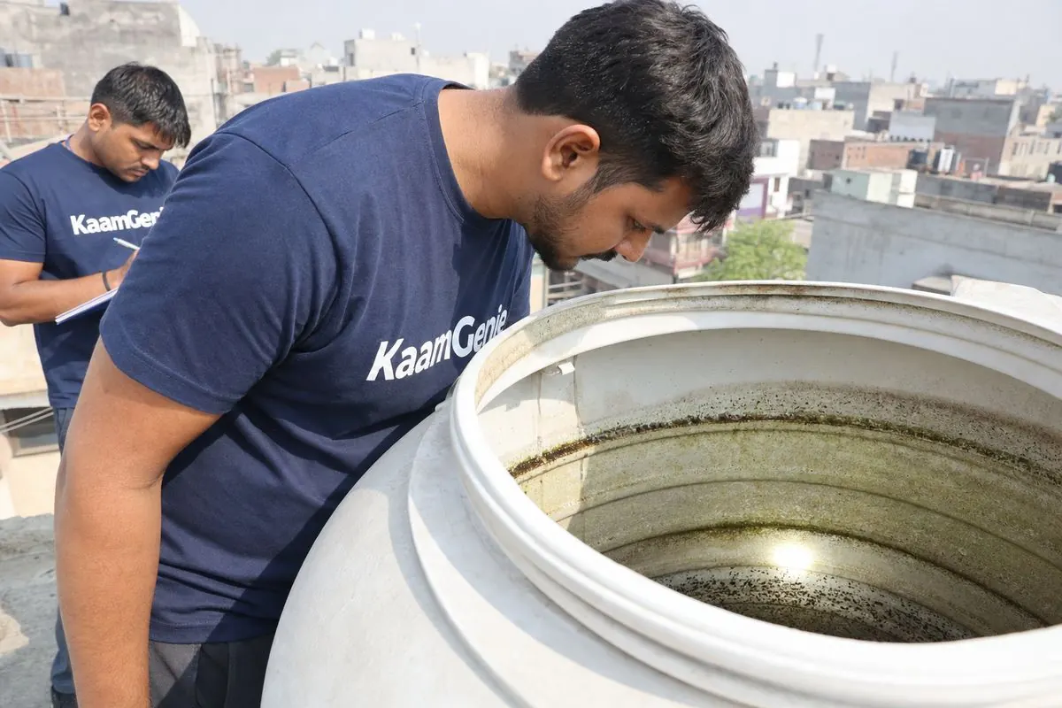 KaamGenie crew lifting the lid of a Delhi rooftop water tank during a move-in cleaning, showing dark sediment at the bottom