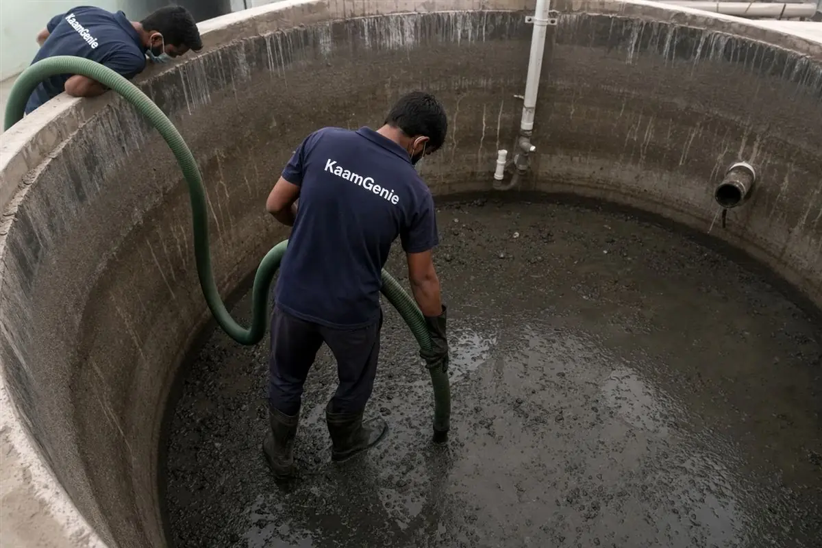 A KaamGenie worker in a navy shirt vacuuming sludge from a drained water tank in Gurgaon